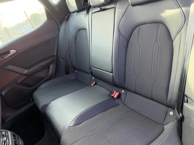 Vue intérieure du siège arrière droit de la SEAT LEON 2025, tissu noir avec coutures apparentes et ceintures rouges.