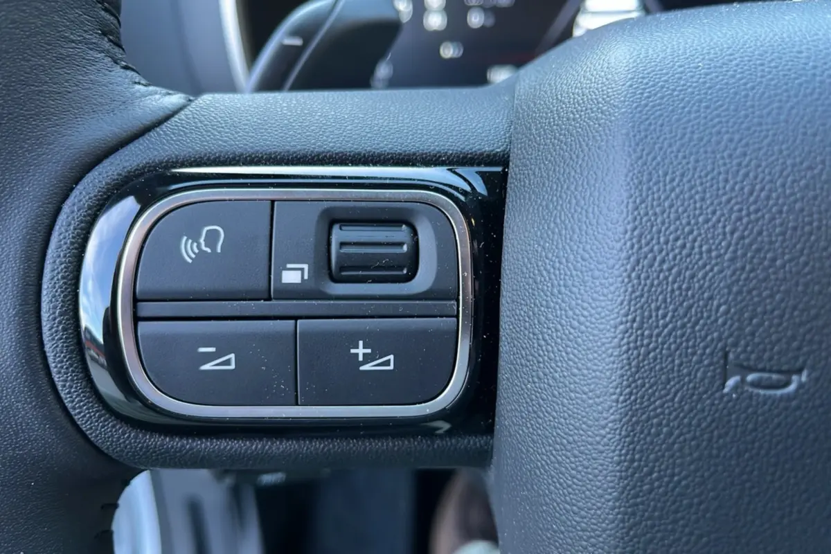 Gros plan sur les commandes vocales et de volume au volant cuir du Citroën C5 Aircross Hybrid blanc okénite.
