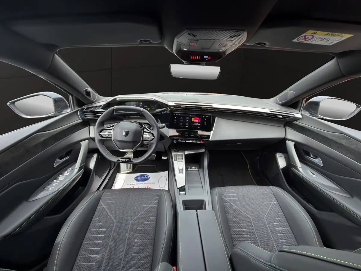 Vue intérieure avant de la Peugeot 308 2026, sièges noirs, tableau de bord moderne avec écran tactile central.