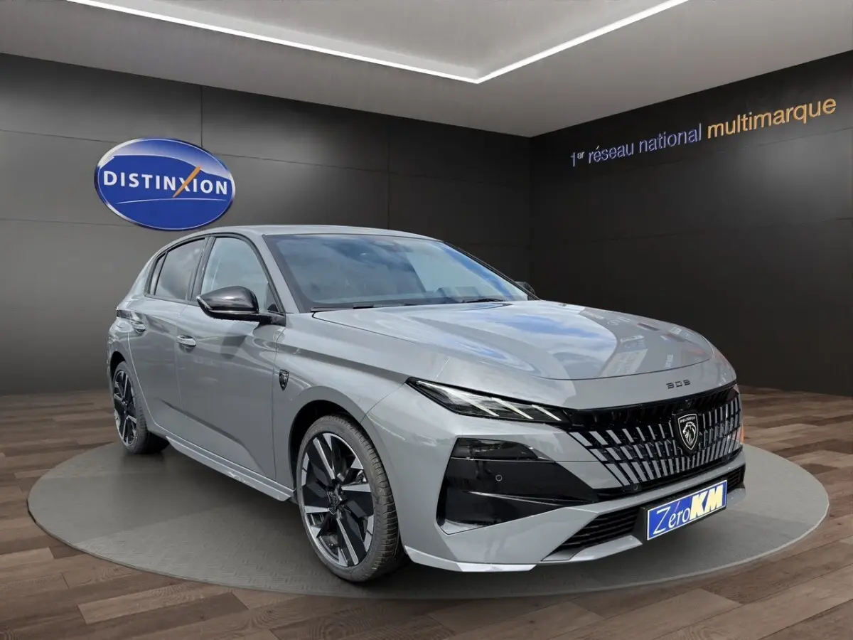 Peugeot 308 gris clair vue 3/4 avant droit, calandre noire distinctive et jantes noires brillantes.