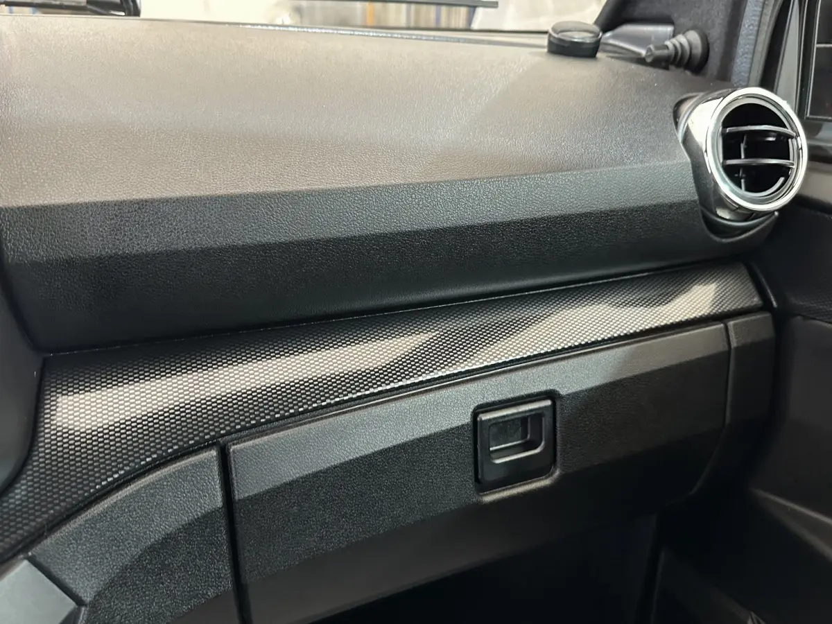 Détail de la planche de bord noire avec insert texturé et sortie d'air ronde côté passager d'une Aixam Ambition rouge.