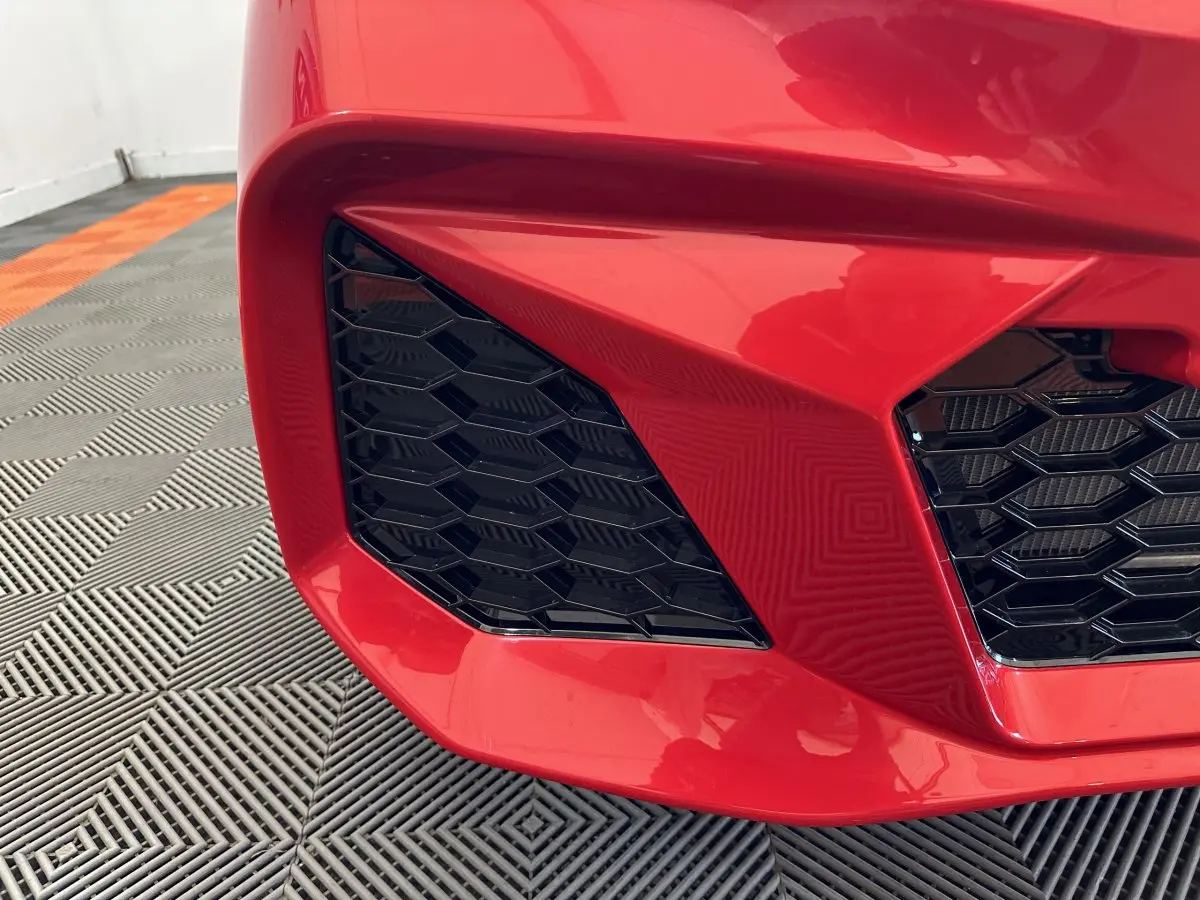 Gros plan sur la calandre avant gauche rouge vif de l'AIXAM AMBITION 0.5 CITY COUPE GTI E5+ 2025 avec grille noire hexagonale.