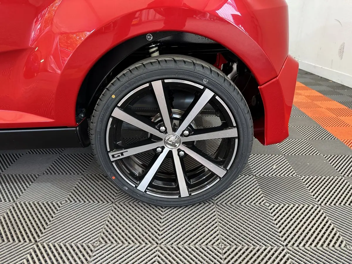 Gros plan sur la roue arrière droite rouge de l'AIXAM AMBITION 0.5 CITY COUPE GTI avec jante noire et argentée marquée GT