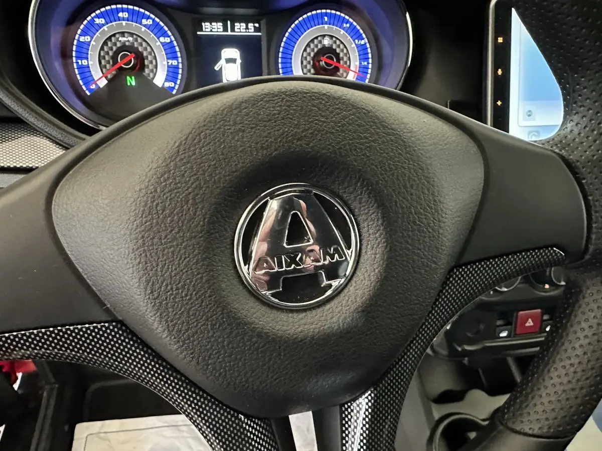 Gros plan sur le volant noir de l'AIXAM AMBITION 0.5 CITY COUPE GTI avec tableau de bord bleu en arrière-plan.