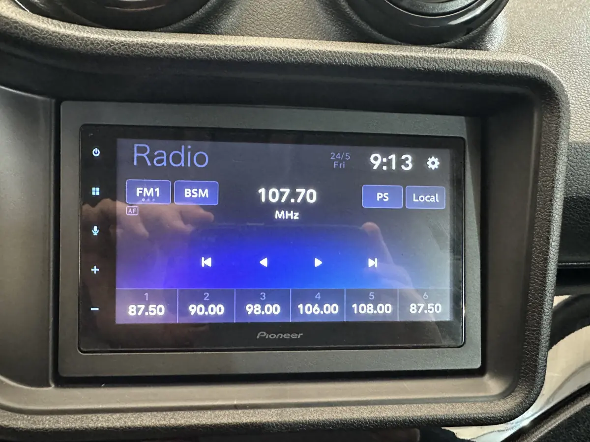 Écran tactile radio Pioneer affichant la fréquence 107.70 MHz dans l'habitacle d'une Aixam Ambition rouge.