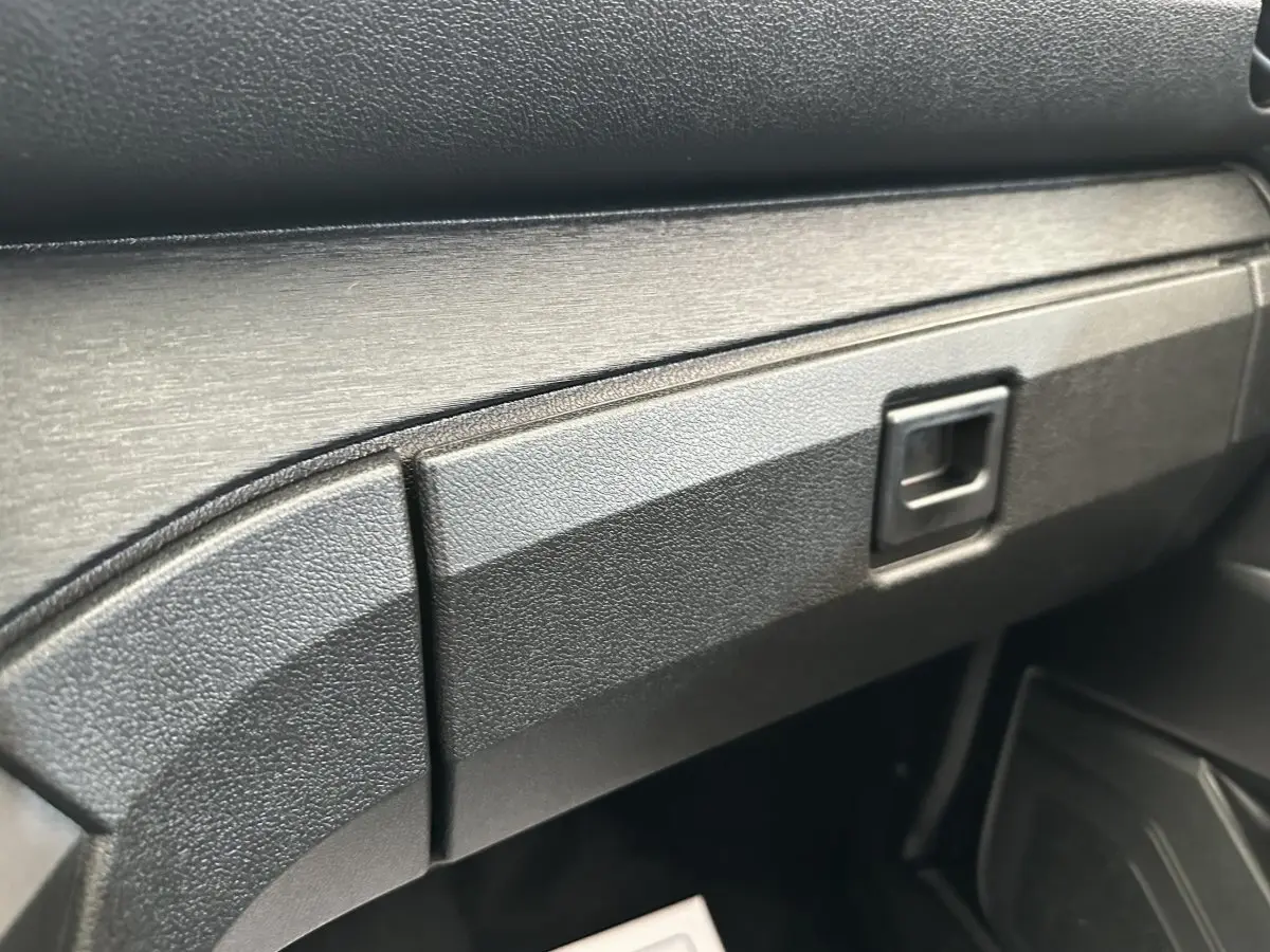 Gros plan sur la boîte à gants noire texturée de l'AIXAM AMBITION 0.5 CITY PACK 2025, intérieur sobre.