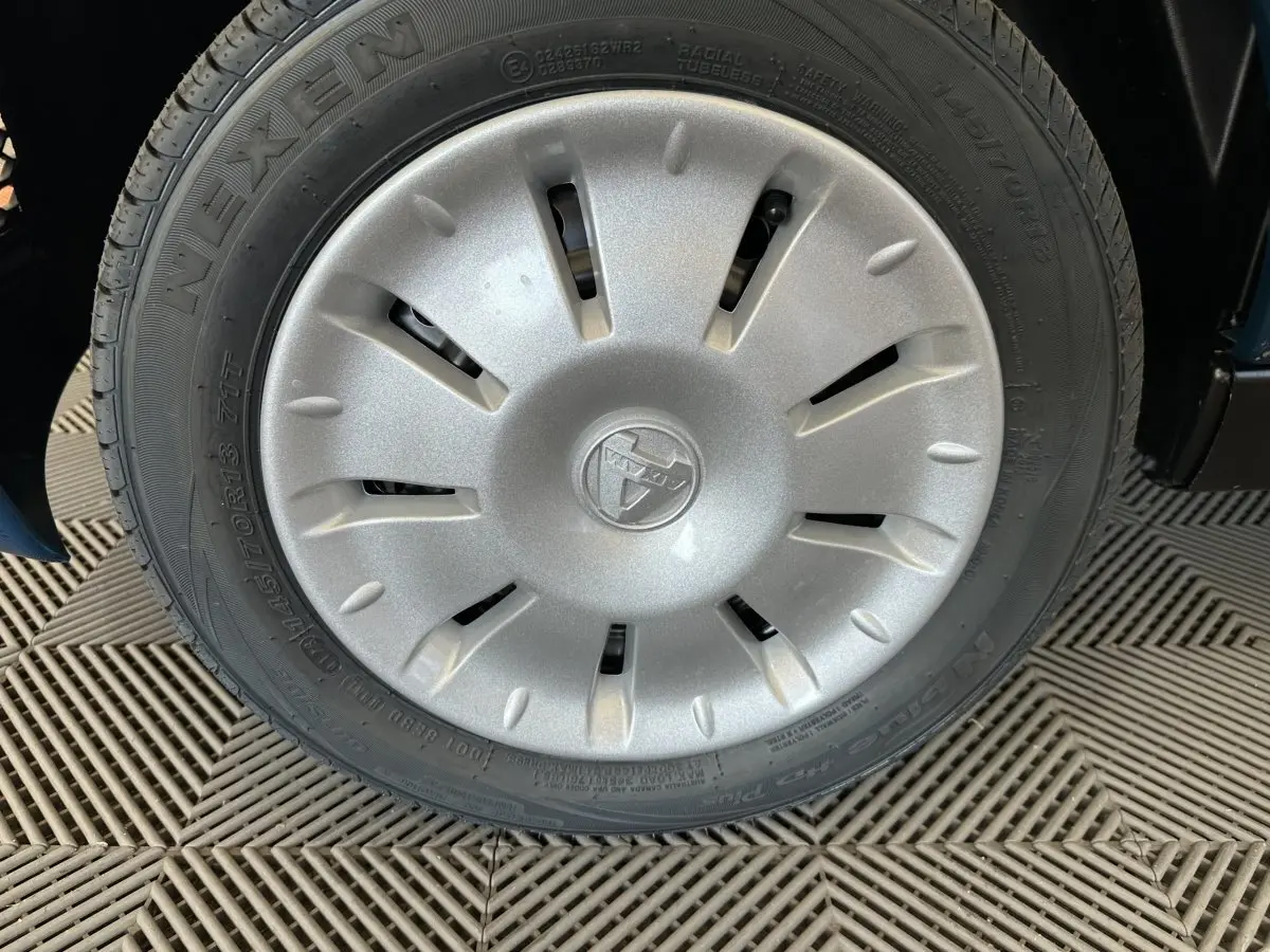 Gros plan sur la roue avant droite d'une Aixam Ambition bleu 2025 avec enjoliveur gris et logo central marqué.