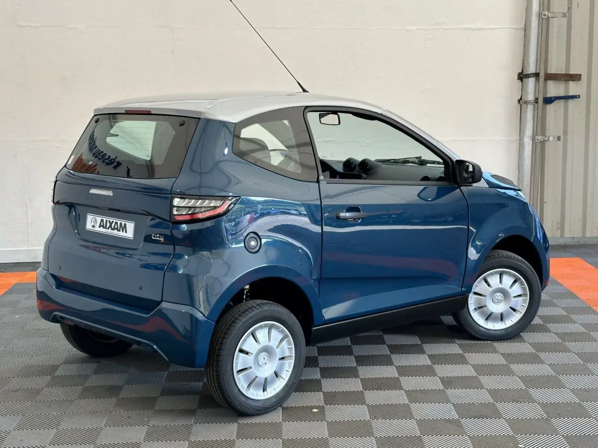 Vue 3/4 arrière droite d'une Aixam Ambition 0.5 City Pack bleu avec toit blanc et rétroviseur caméra côté gauche.