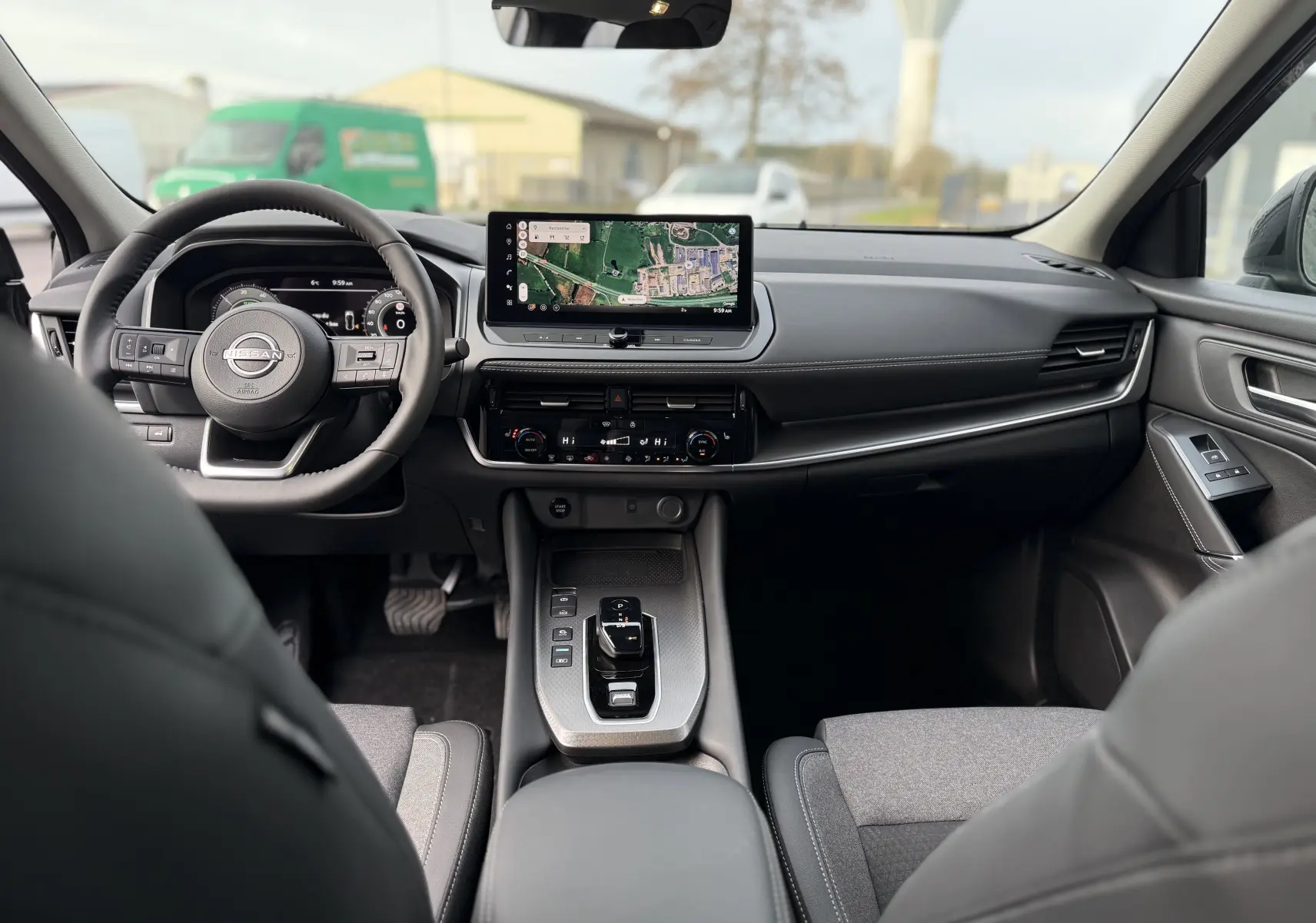 Vue intérieure avant du Nissan Qashqai 1.5 E-POWER 2025, tableau de bord noir avec écran tactile central et volant multifonction.