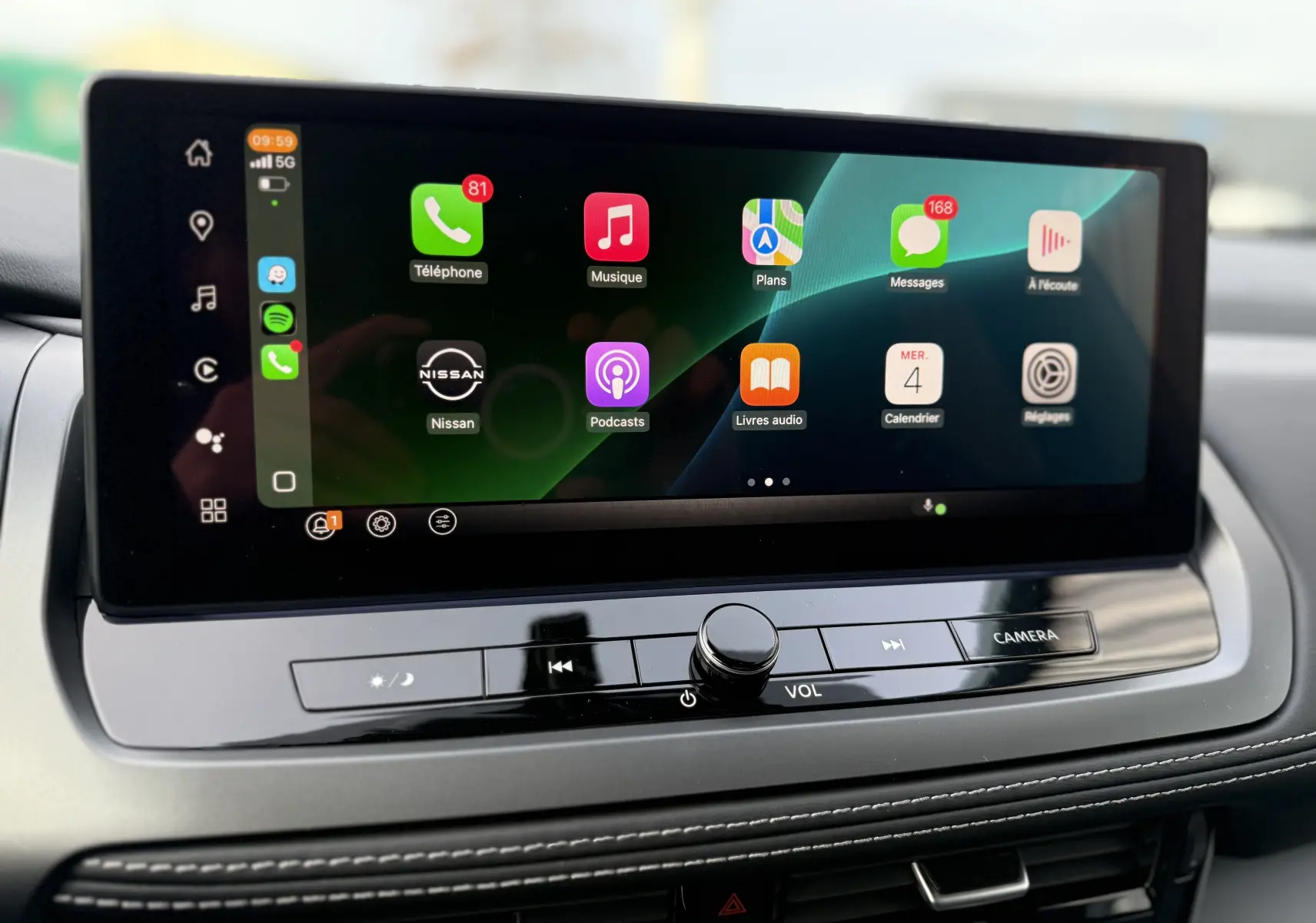 Écran tactile central du Nissan Qashqai 2025 affichant les applications connectées, avec commandes volume et caméra en dessous.