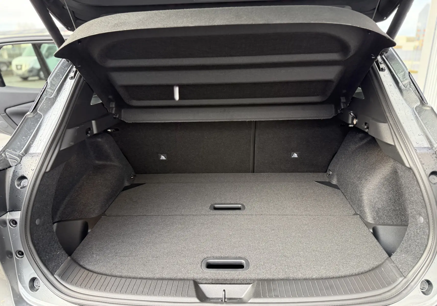 Coffre ouvert vu de l'arrière d'un Nissan Qashqai 1.5 E-POWER gris squale metal, espace de chargement plat et spacieux.