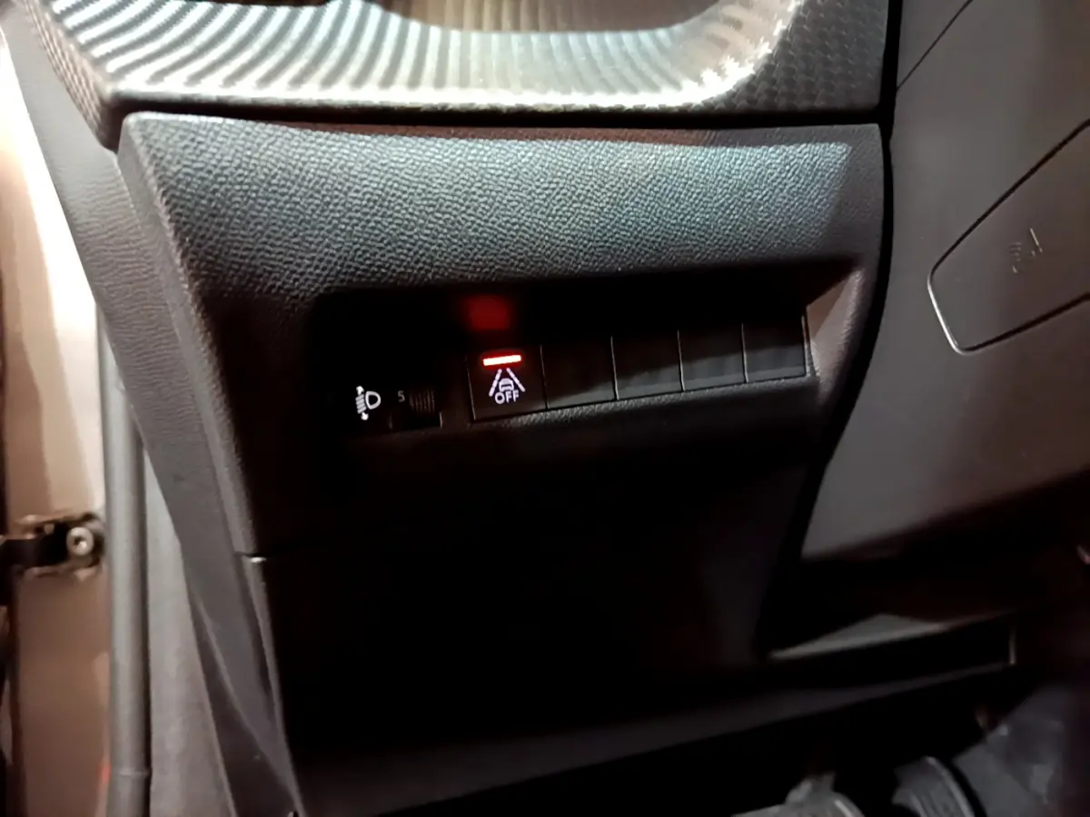 Détail intérieur côté gauche du tableau de bord d’une Peugeot 208 gris foncé, bouton d’aide à la conduite désactivée allumé.