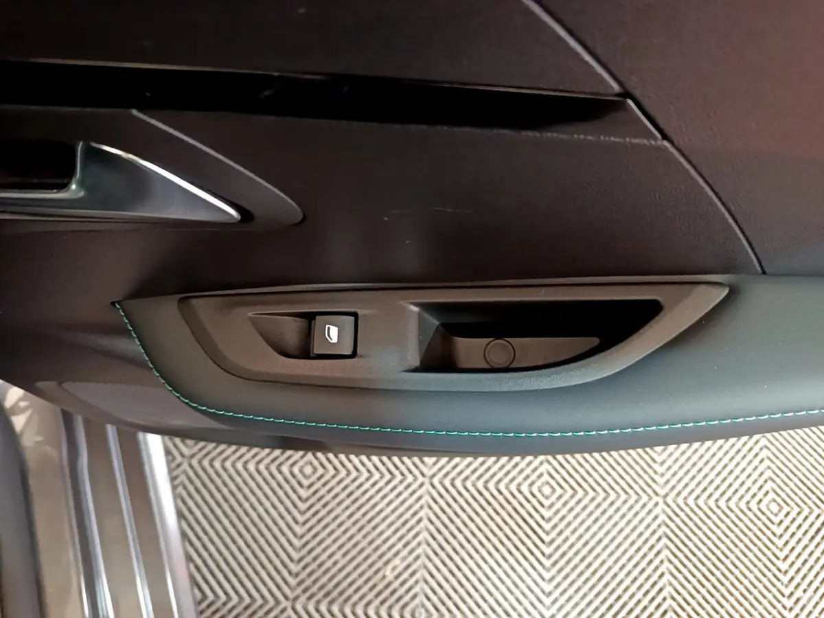 Gros plan sur la poignée intérieure de porte côté conducteur d'une Peugeot 208 gris foncé avec surpiqûres bleues.