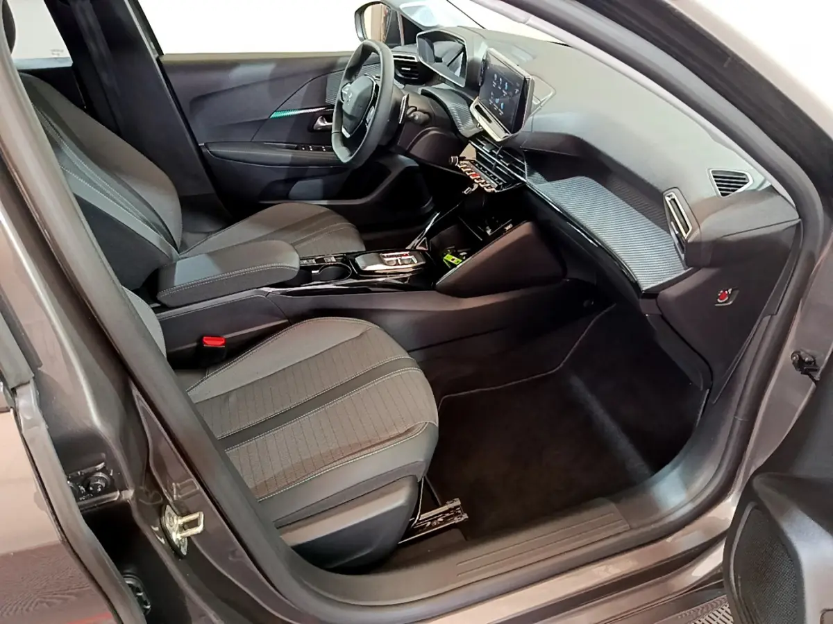 Vue intérieure côté conducteur de la Peugeot 208 gris foncé 2022, avec tableau de bord digital et sièges tissu noirs.