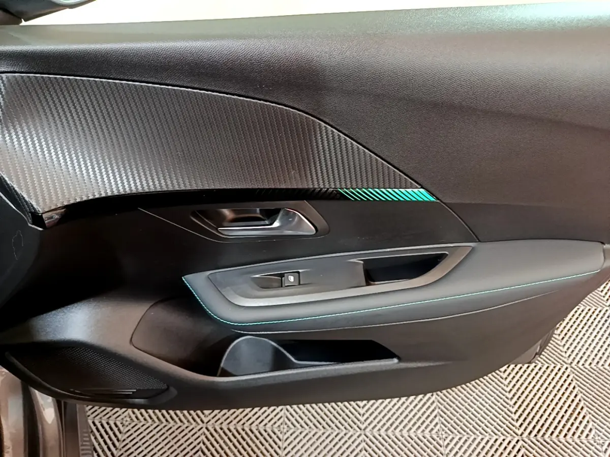 Gros plan sur la porte intérieure côté gauche de la Peugeot 208 gris foncé avec surpiqûres bleues et insert décoratif.