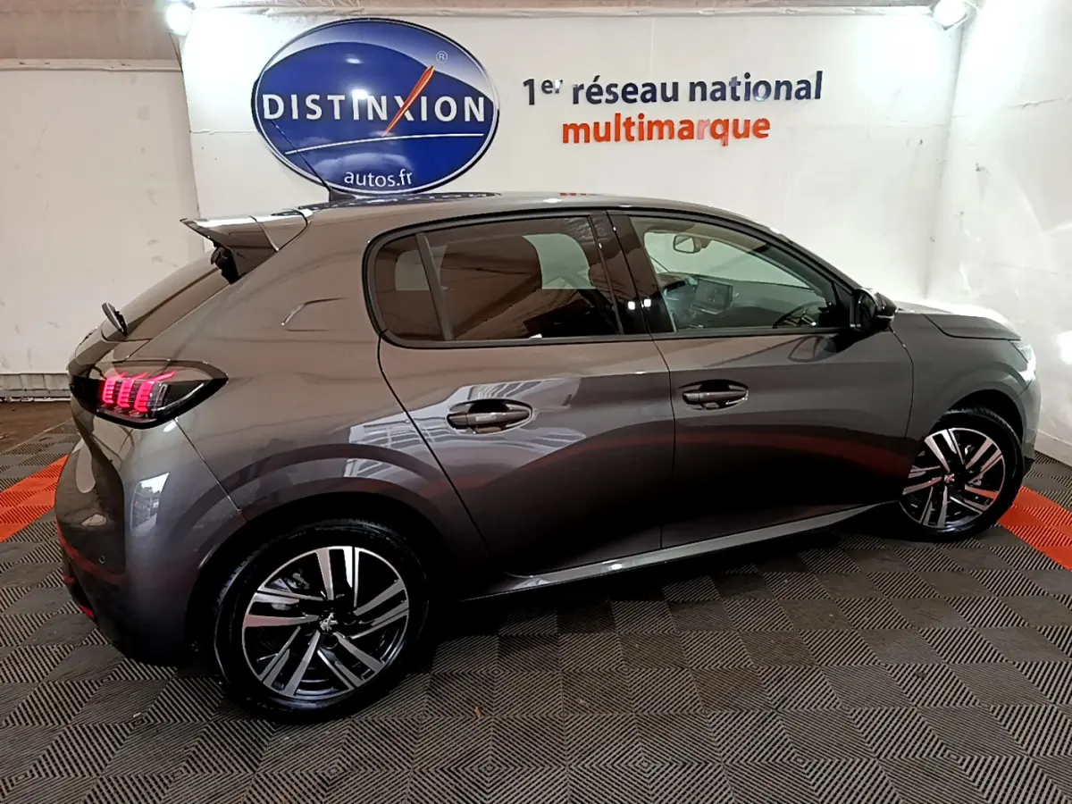 Peugeot 208 gris foncé vue de profil droit en intérieur, feux arrière LED et jantes alliage visibles.