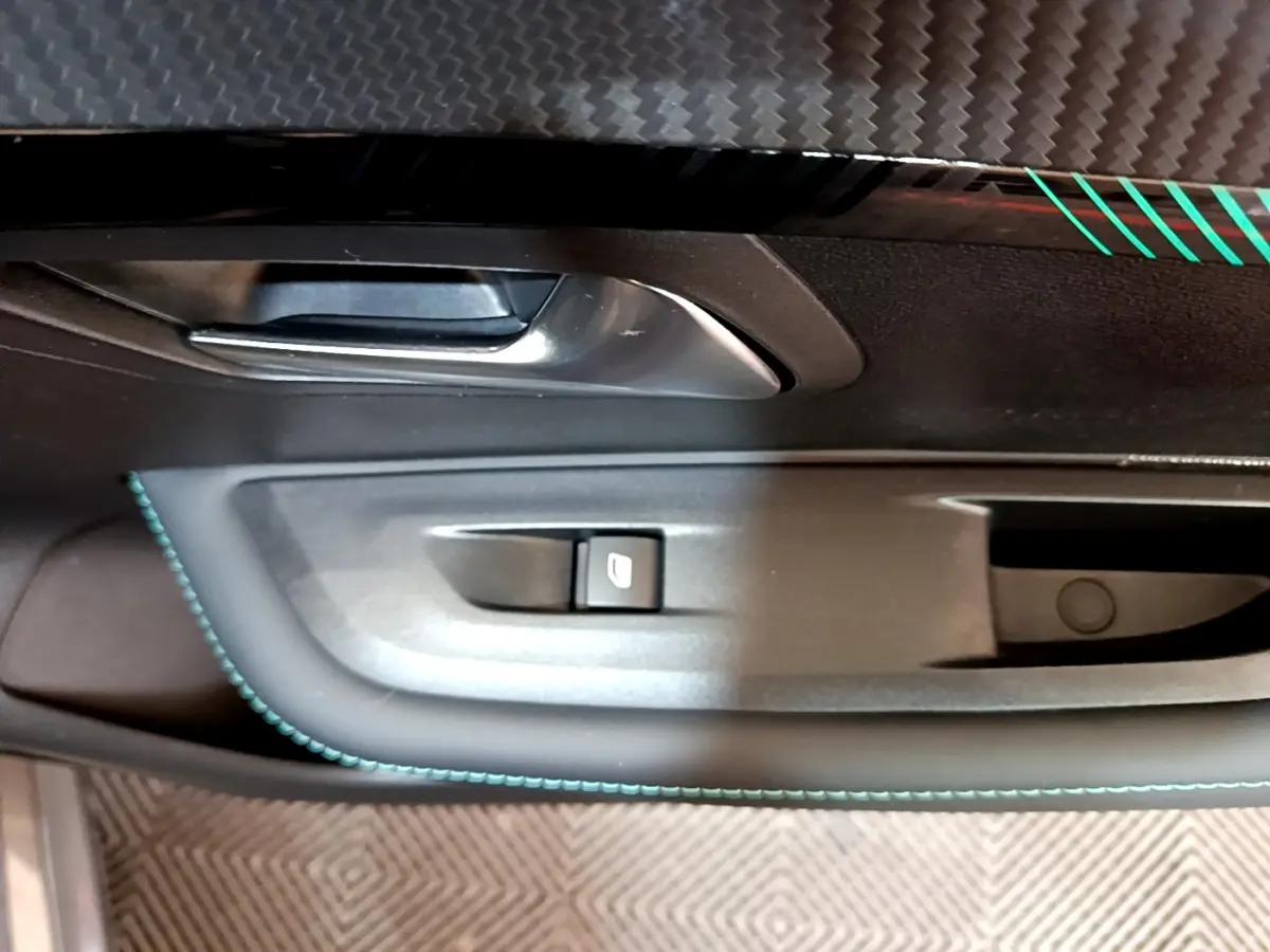 Gros plan sur la poignée intérieure et commande de vitre côté conducteur de la Peugeot 208 gris foncé avec surpiqûres bleues.