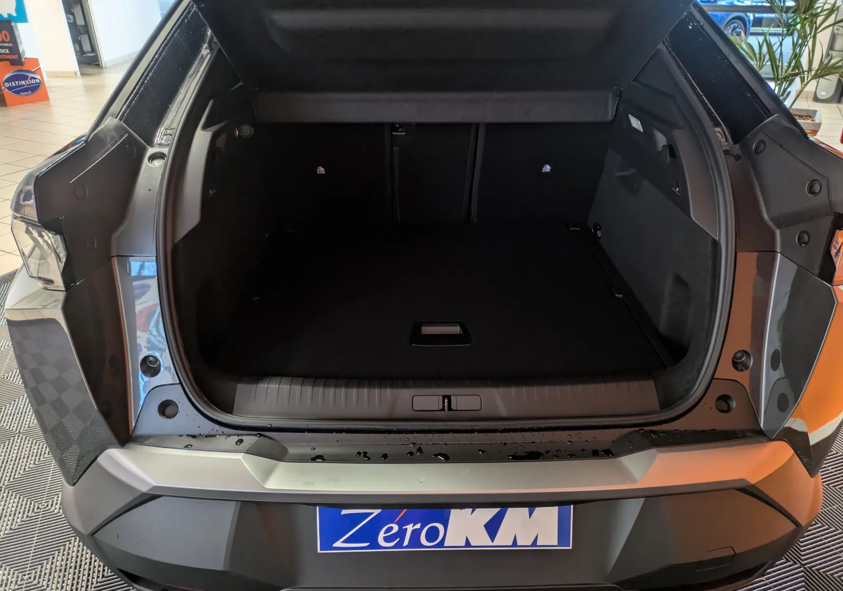 Coffre ouvert vu de l'arrière d'un Peugeot 3008 Hybrid 145 gris titane toit noir dans un showroom.