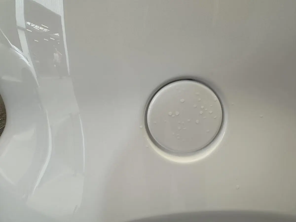 Gros plan sur la trappe de recharge blanche de l'AIXAM MINAUTO E ACCESS 2025 côté conducteur avec reflets et gouttes d'eau.