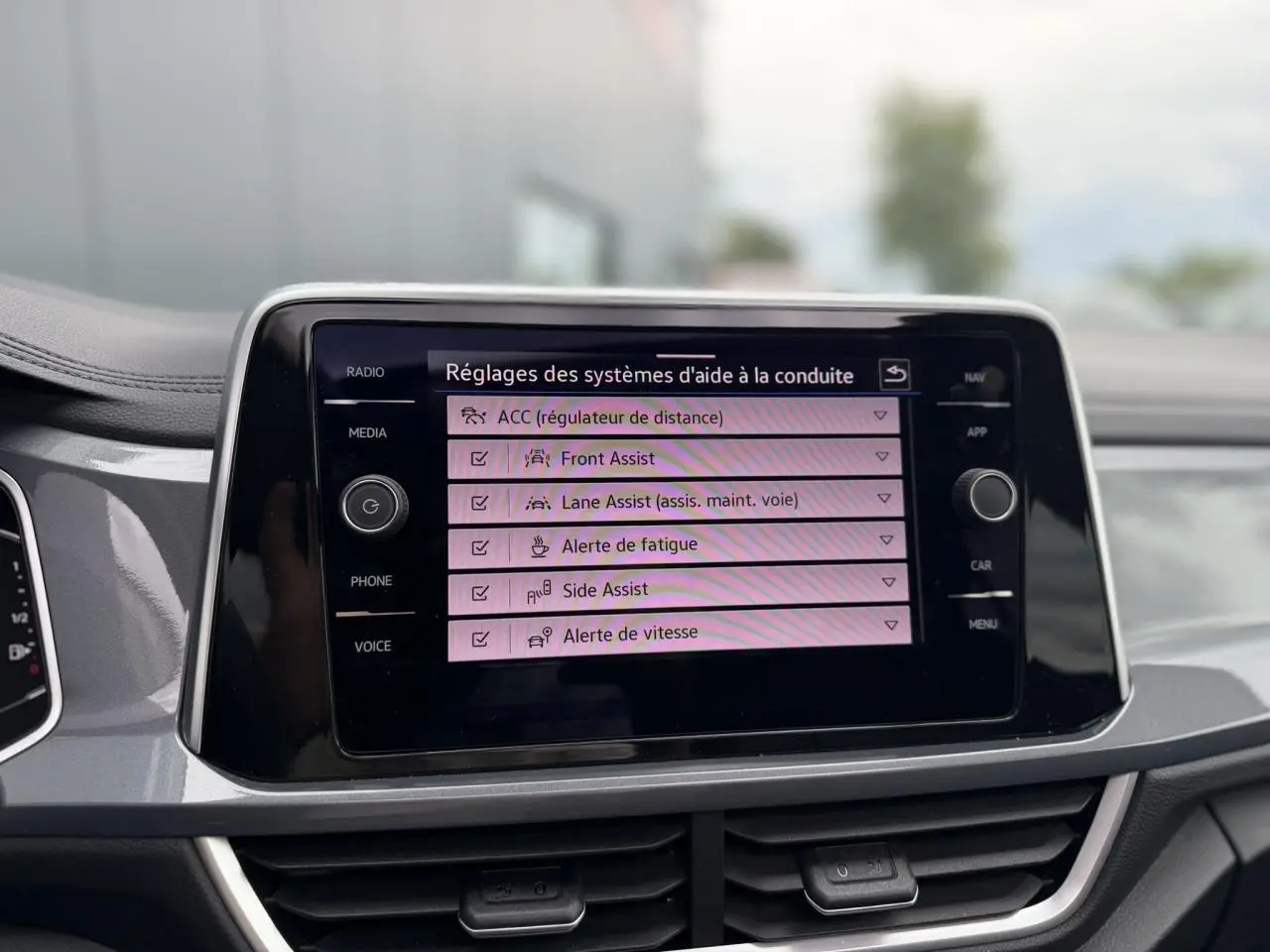 Écran tactile central du Volkswagen T-Roc 2024 affichant les réglages des aides à la conduite, tableau de bord gris argent.