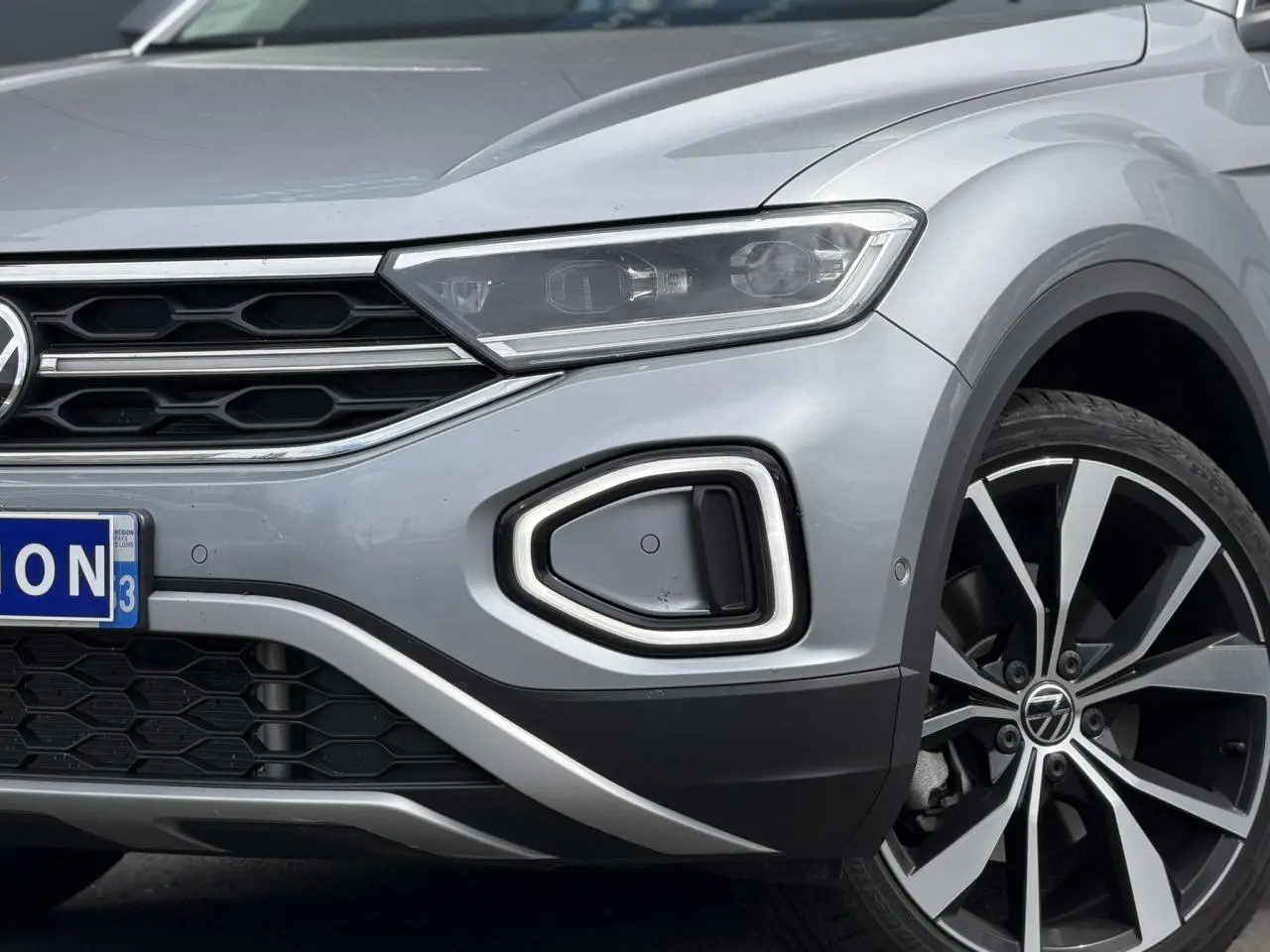 Gros plan sur l'avant droit du Volkswagen T-Roc argent Pyrite, mettant en valeur le phare LED et la jante alliage 19 pouces.