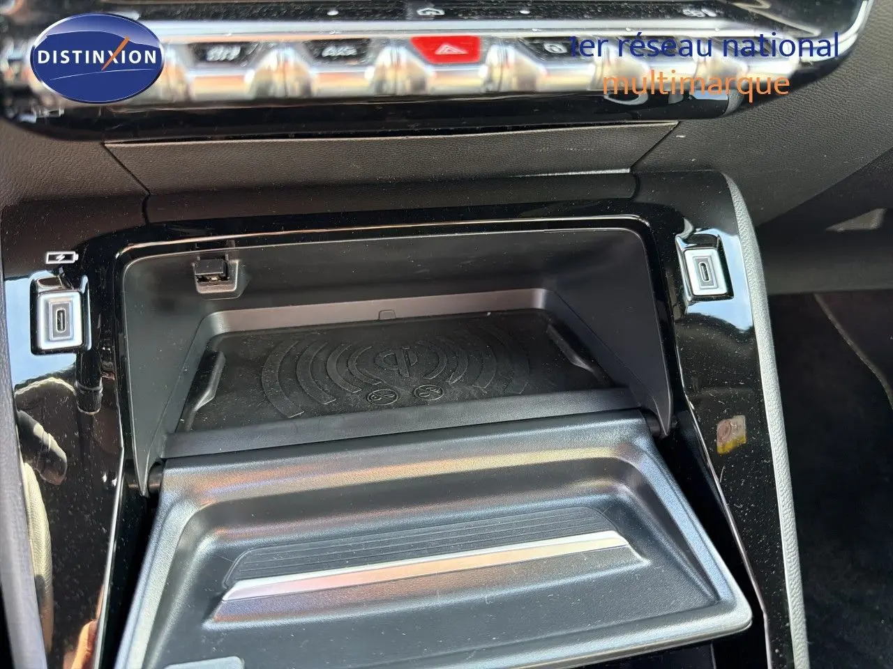 Gros plan sur la console centrale du Peugeot 2008 1.2 HYBRID 145 GT, montrant un compartiment de rangement avec chargeur sans fil.