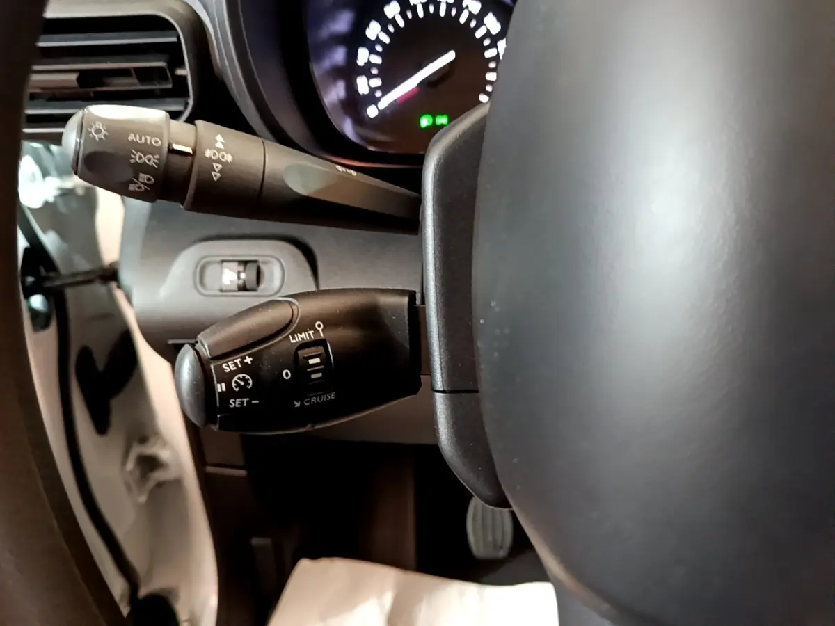 Gros plan sur la commande de régulateur de vitesse à gauche du volant du Citroën Berlingo blanc, tableau de bord en arrière-plan.