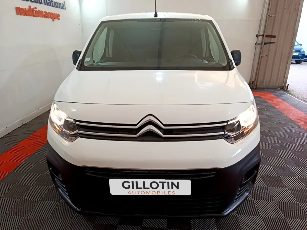 Vue frontale d'un Citroën Berlingo blanc 2021 avec phares allumés et pare-chocs noir dans un showroom.