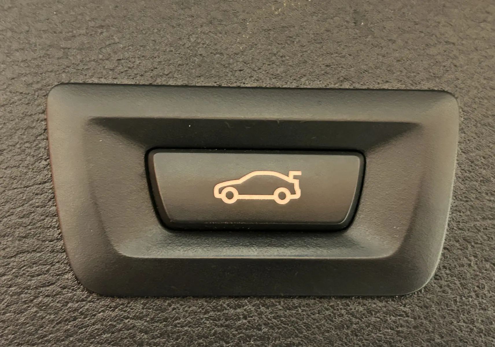 Bouton noir avec icône lumineuse orange représentant l'ouverture du coffre d'un BMW X3 sDrive18dA 2017.