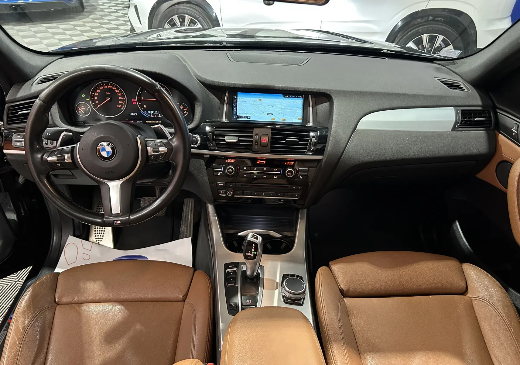 Vue intérieure avant du BMW X3 sDrive18dA 2017, avec sièges cuir marron et tableau de bord noir intégrant un écran GPS.