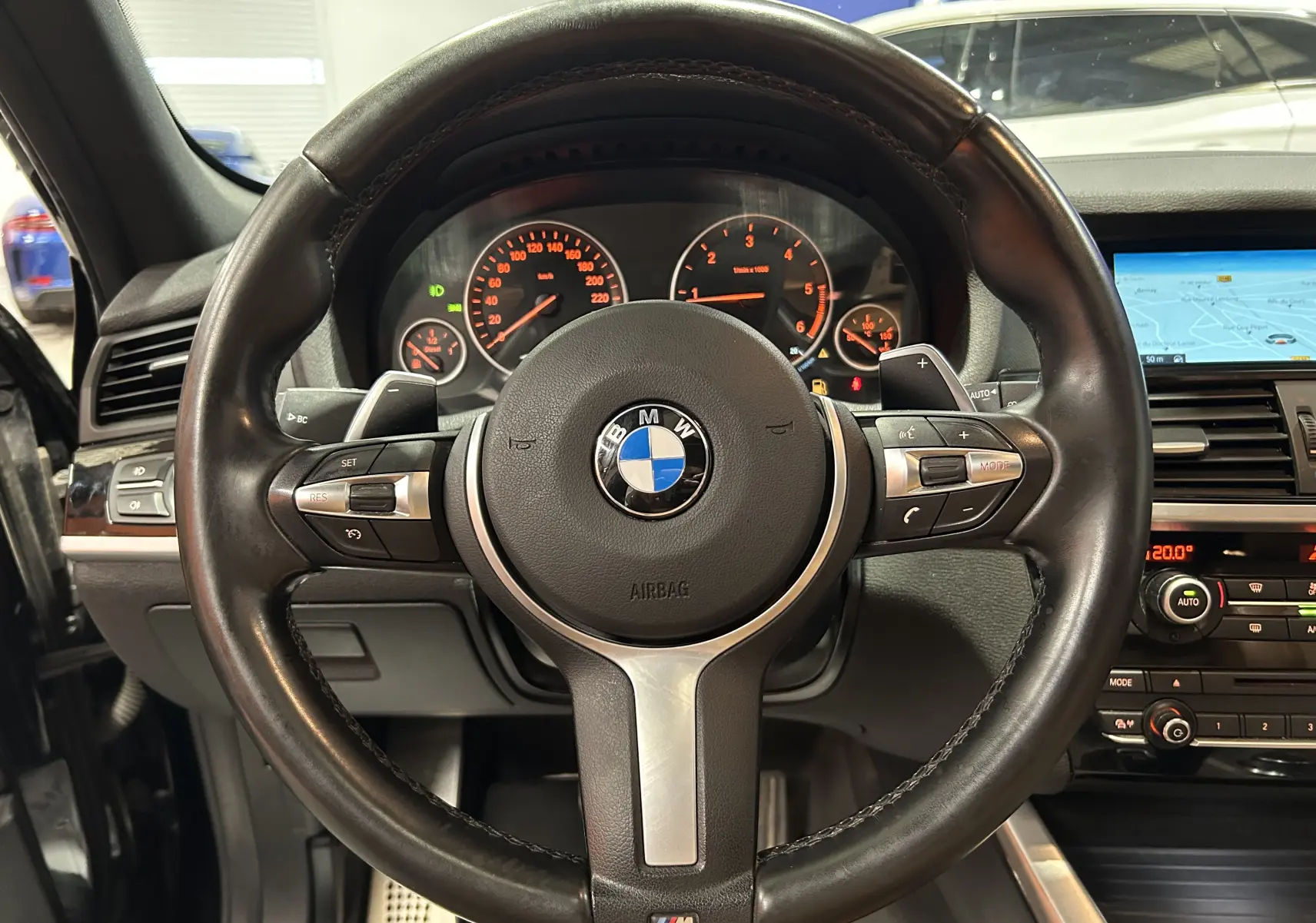 Vue intérieure centrée sur le volant cuir noir BMW M avec tableau de bord et écran de navigation allumés.