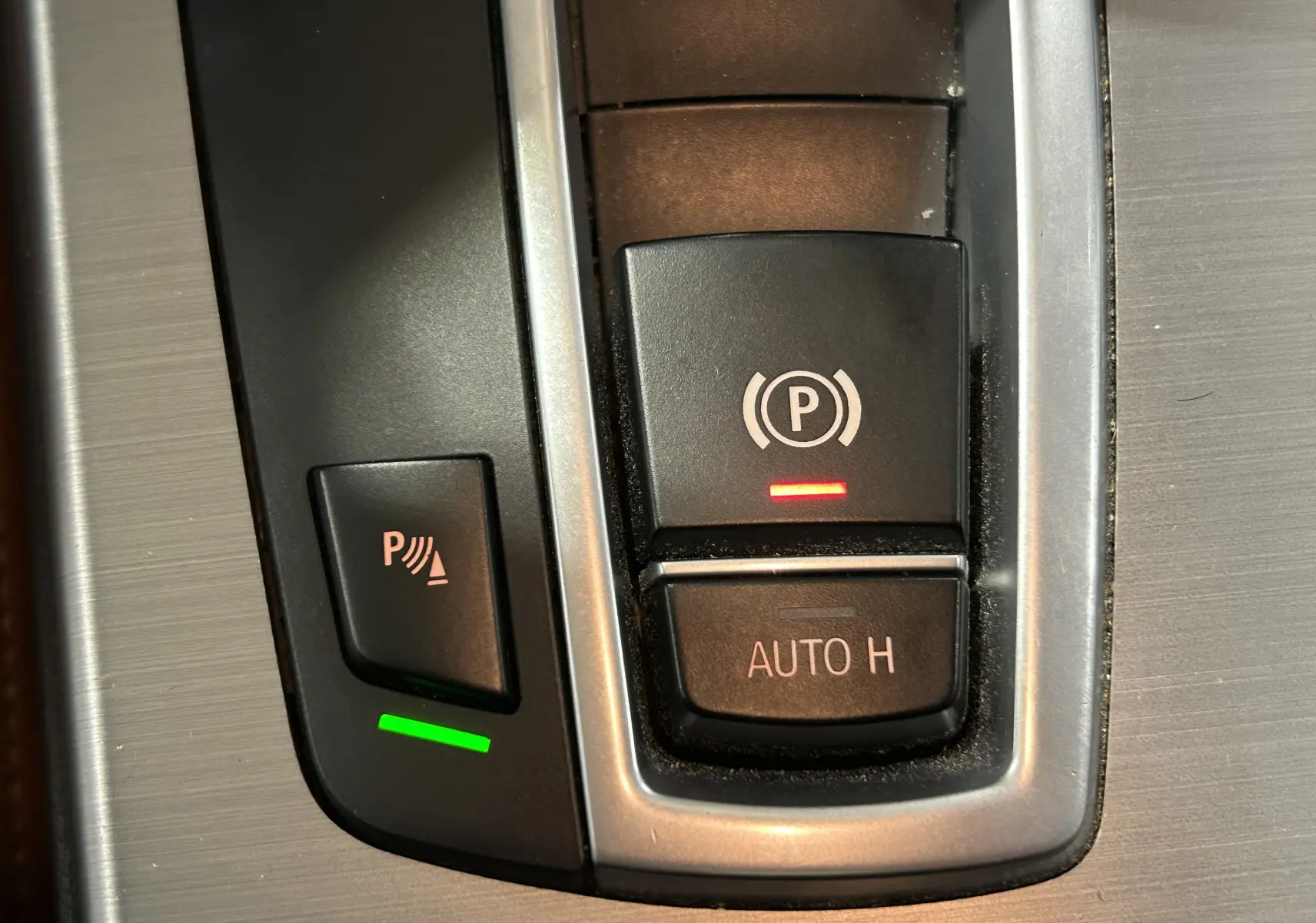 Gros plan sur les boutons de commande du frein à main électrique et de l’aide au stationnement dans une BMW X3 noire de 2017.