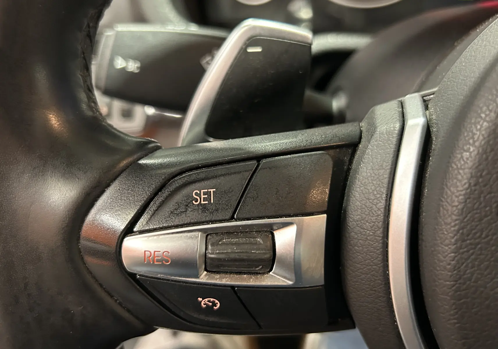 Gros plan sur les commandes de régulateur de vitesse sur le volant cuir noir du BMW X3 sDrive18dA 2017.