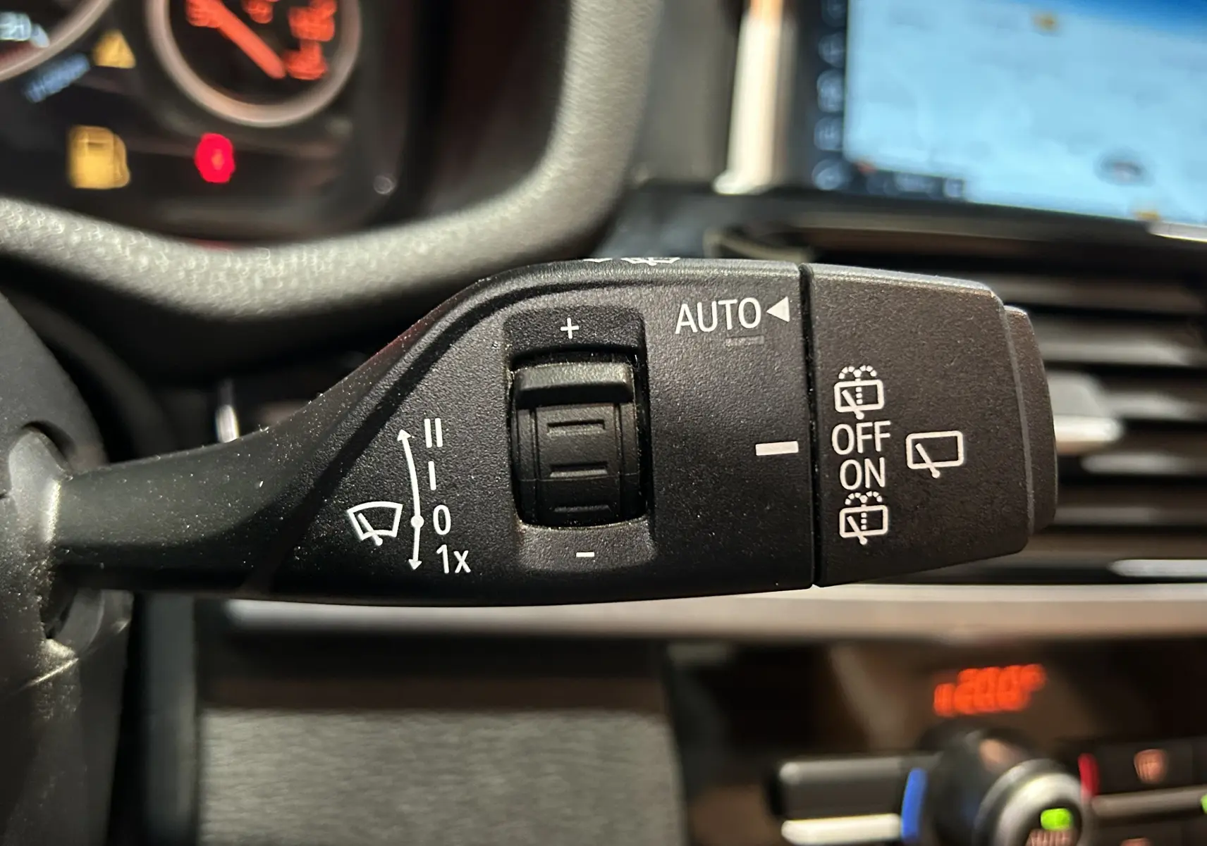 Gros plan sur le commodo d'essuie-glace noir dans l'habitacle d'une BMW X3 2017, avec tableau de bord flou en arrière-plan.