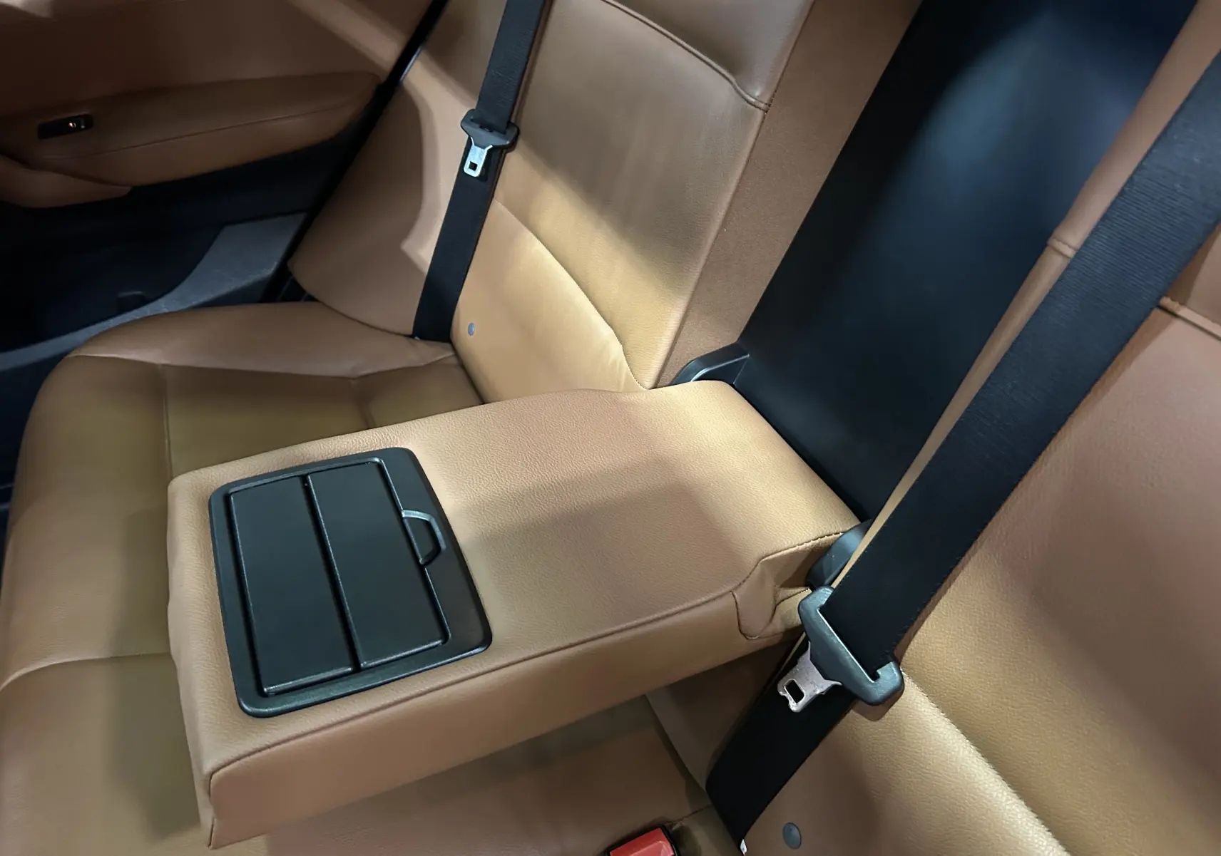 Vue rapprochée de la banquette arrière en cuir marron du BMW X3, avec accoudoir central déployé et ceintures noires.