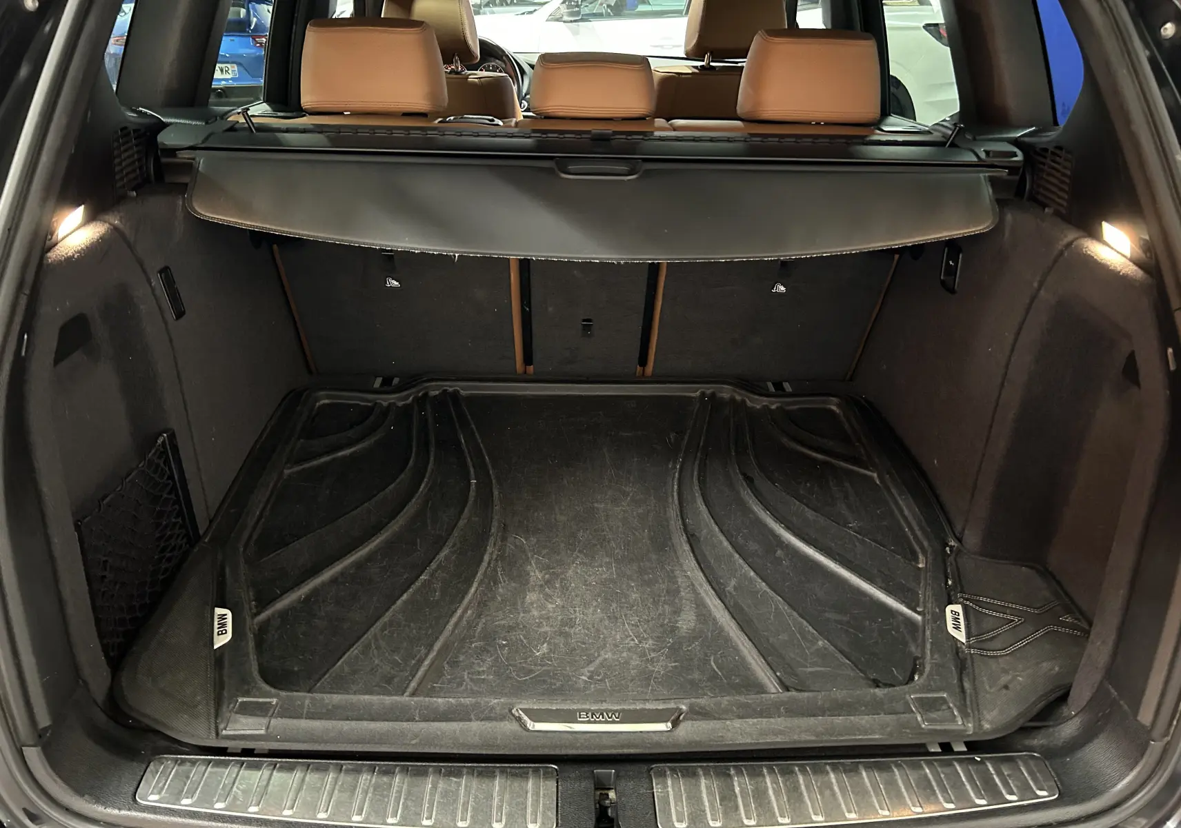 Coffre ouvert vu de l'arrière d'un BMW X3 noir avec tapis de coffre BMW et sièges arrière en cuir marron.