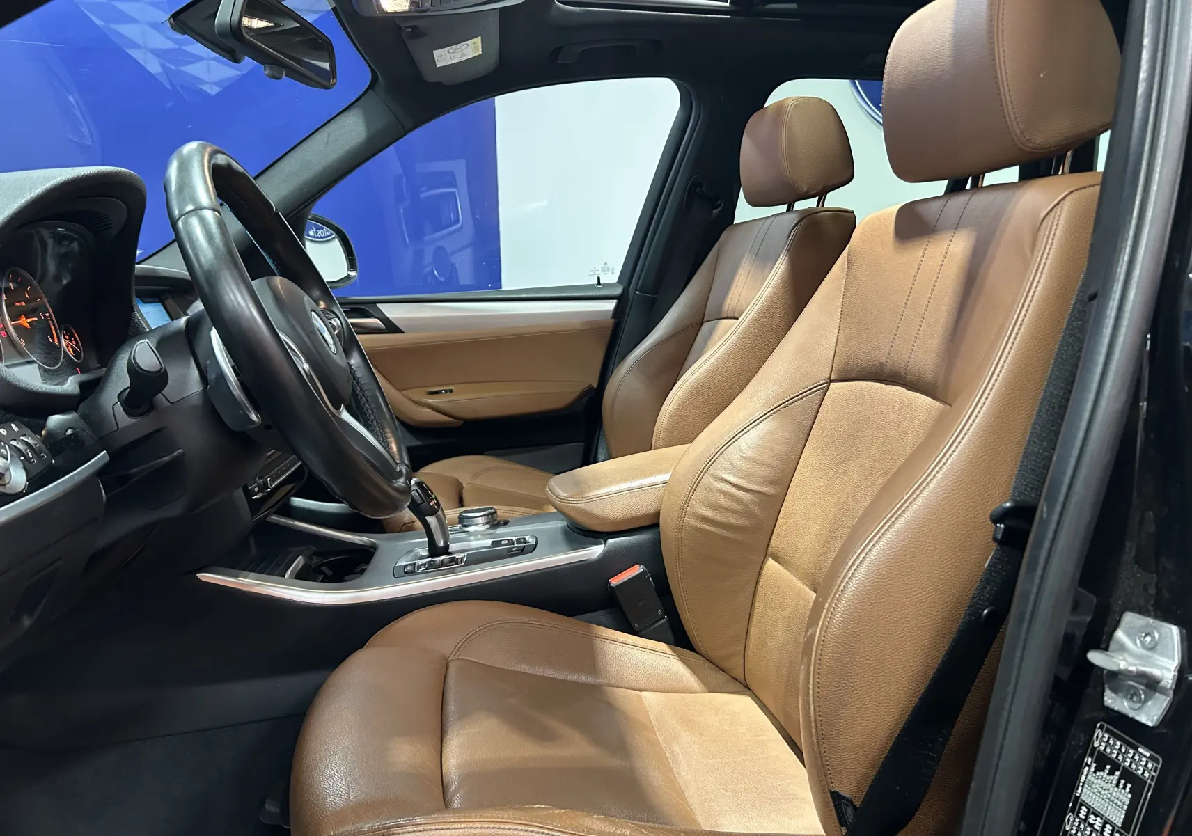 Vue intérieure côté conducteur d'une BMW X3 2017 avec sièges en cuir marron et volant multifonction noir.