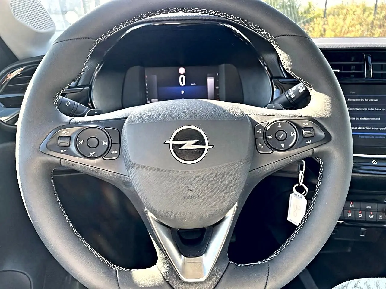 Vue rapprochée du volant sport noir avec surpiqûres blanches de l'Opel Corsa 2025, tableau de bord et écran tactile en arrière-plan.