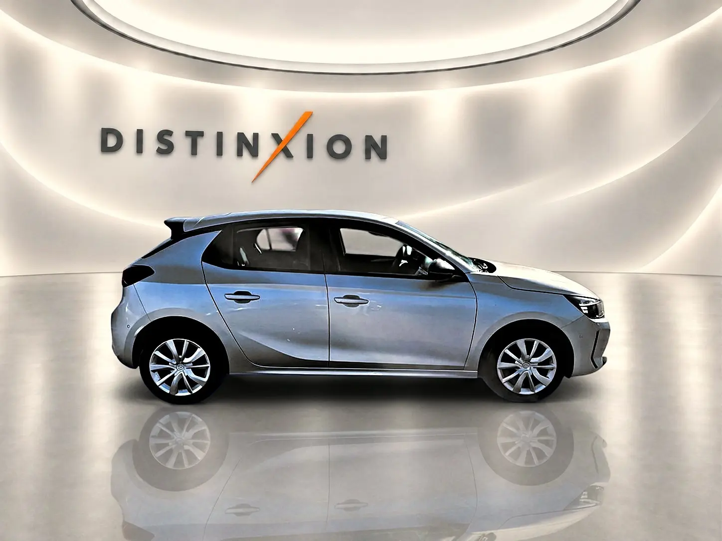 Opel Corsa gris alu vue de profil côté gauche dans un showroom avec reflet au sol et logo Distinxion en arrière-plan.