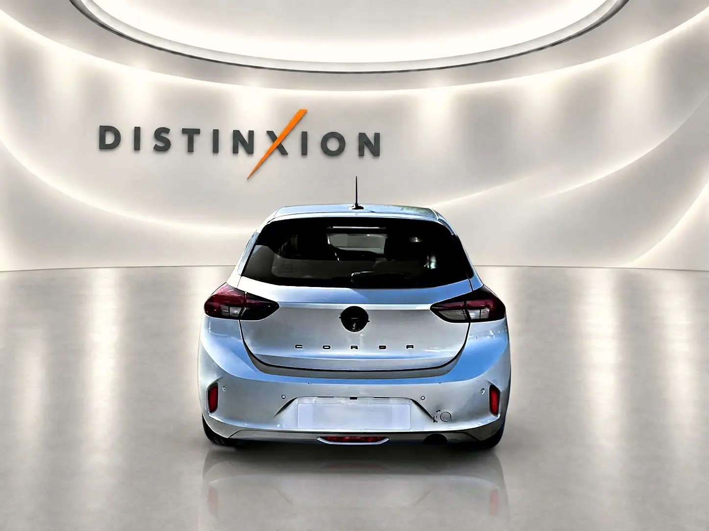 Vue arrière d'une Opel Corsa gris alu 2025 dans un showroom avec logo Distinxion en arrière-plan.