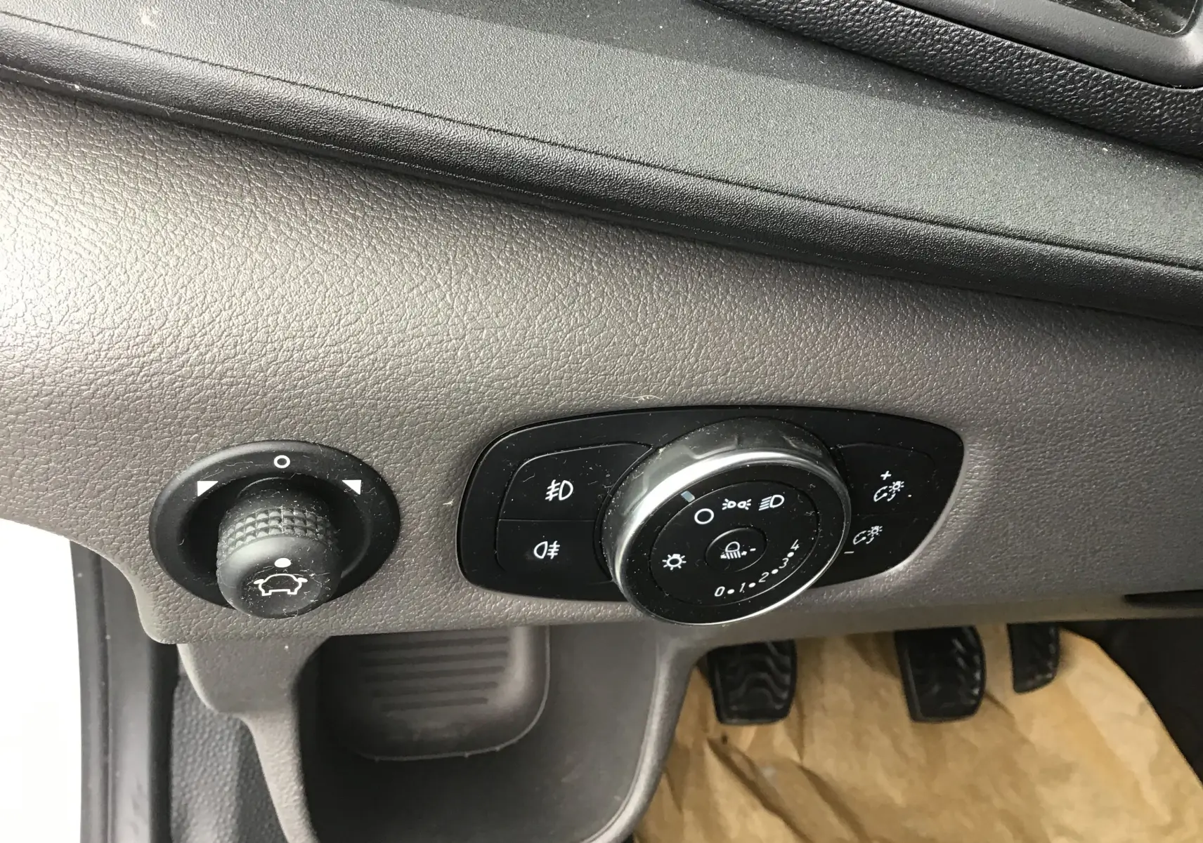 Gros plan sur les commandes d'éclairage et de réglage du tableau de bord du Ford Transit Fourgon blanc, côté conducteur.