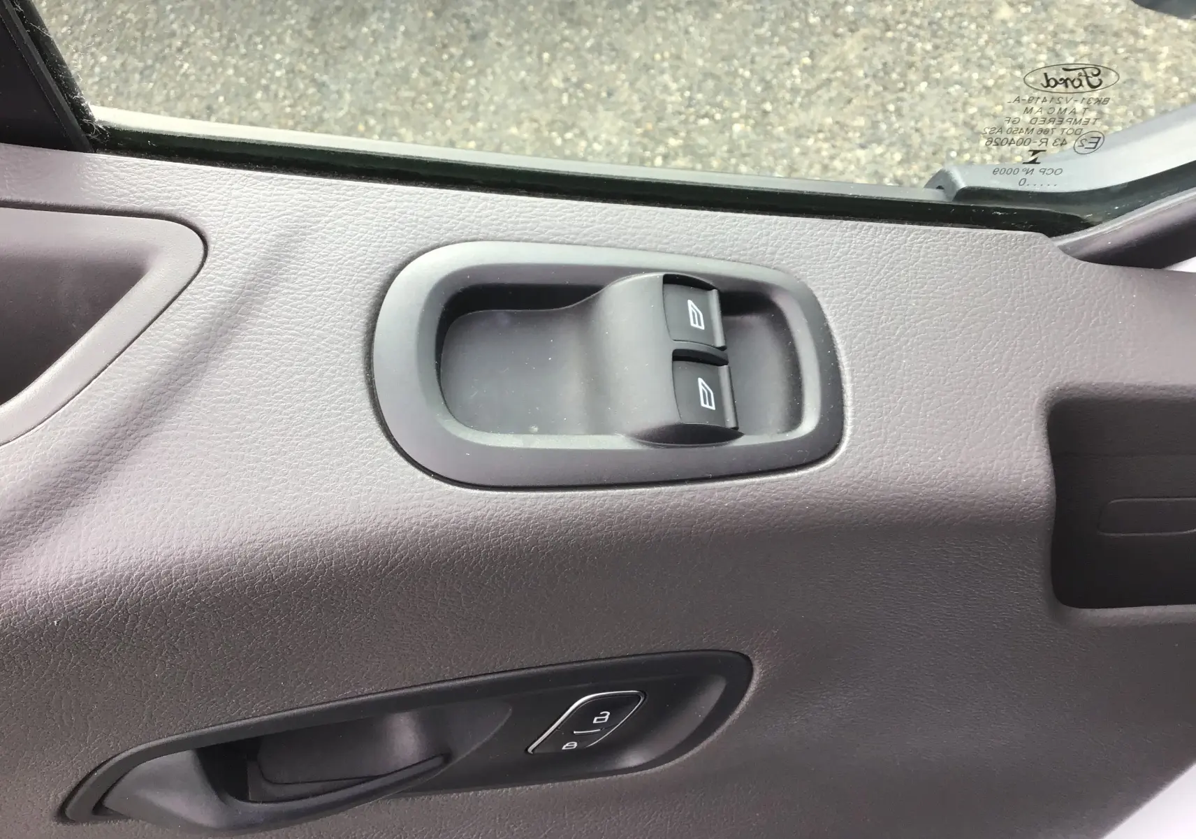 Gros plan sur la porte côté conducteur du Ford Transit Fourgon blanc, montrant les commandes des vitres électriques et la poignée intérieure.