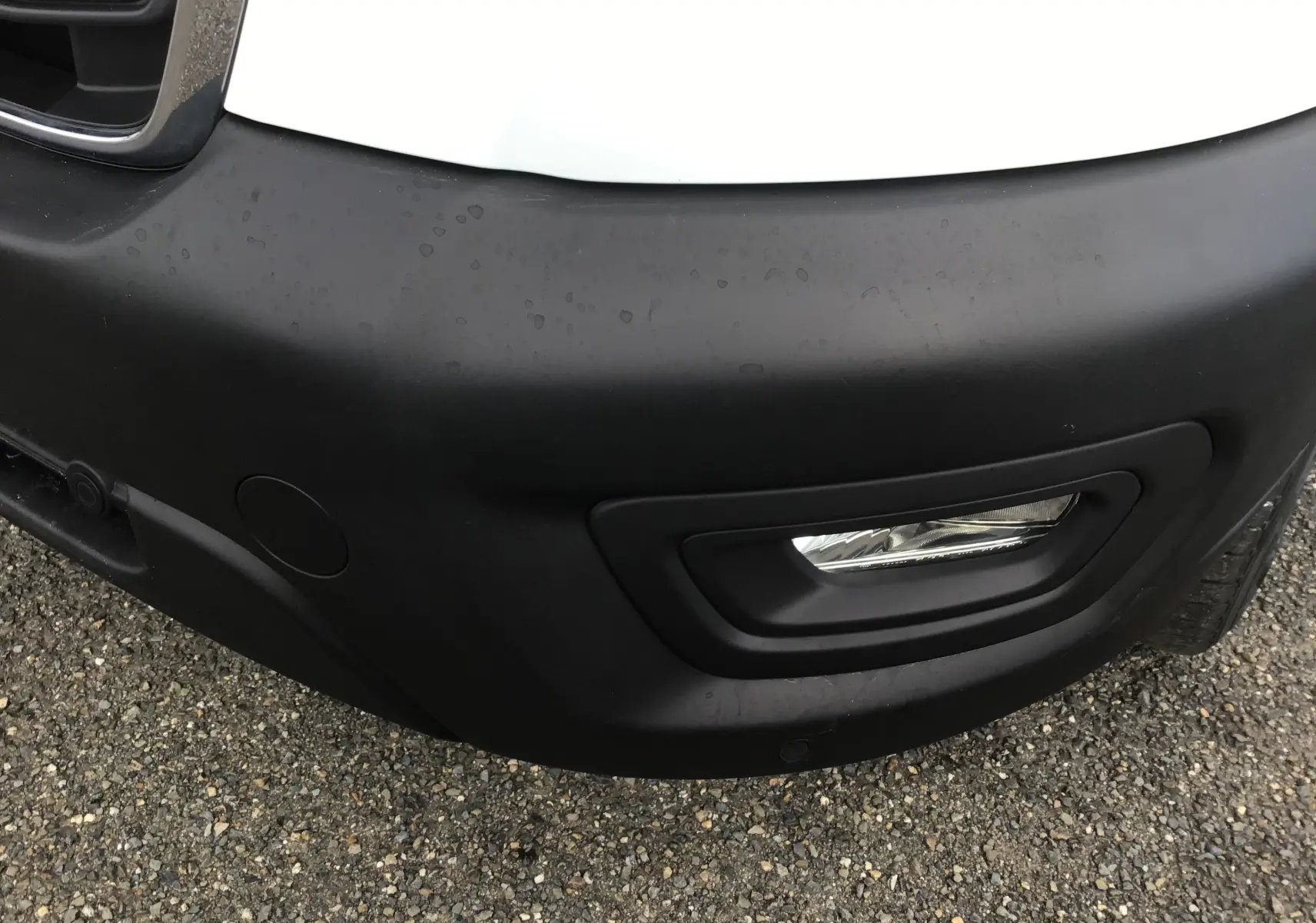 Gros plan sur le pare-chocs avant droit noir et antibrouillard du fourgon Ford Transit blanc de 2020.