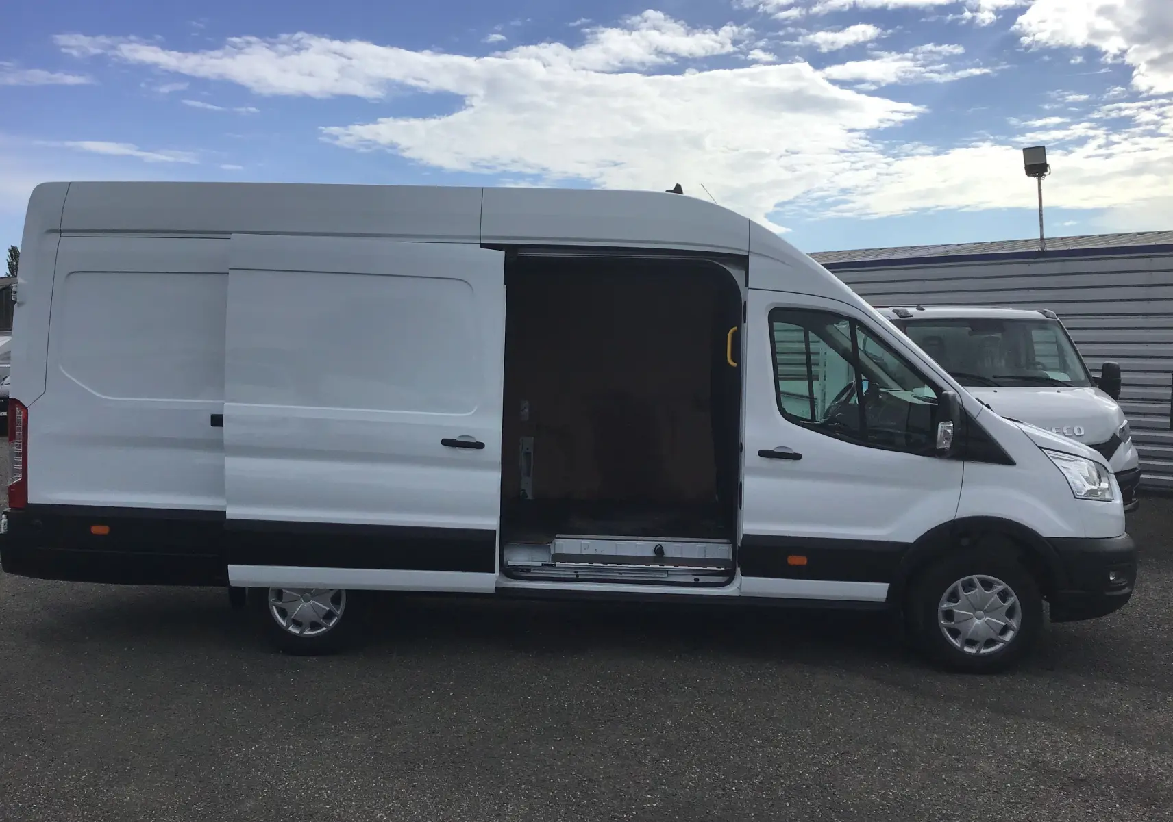 Vue de profil côté gauche d'un fourgon Ford Transit blanc 2020 avec porte latérale coulissante ouverte montrant l'intérieur vide.
