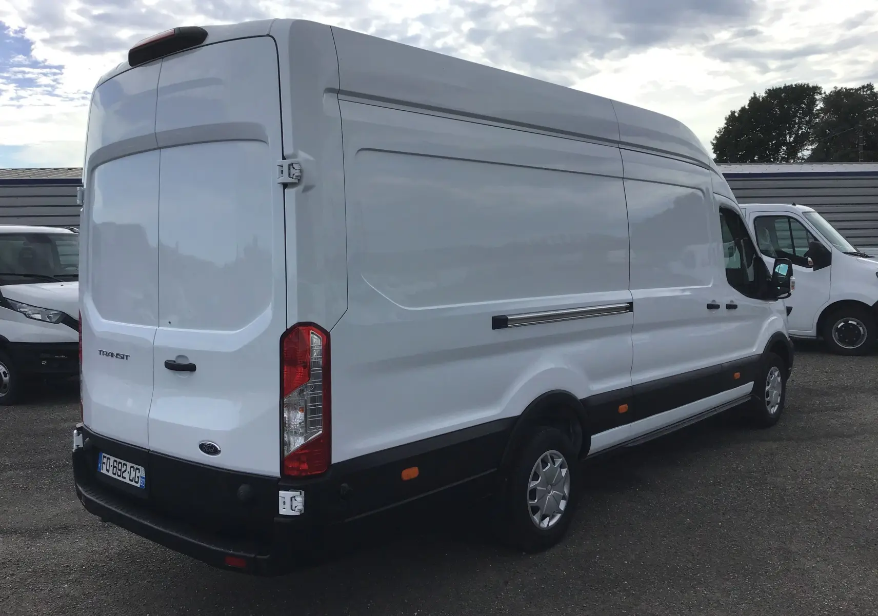 Ford Transit Fourgon blanc vu en 3/4 arrière droit, avec porte arrière fermée et feux rouges verticaux.
