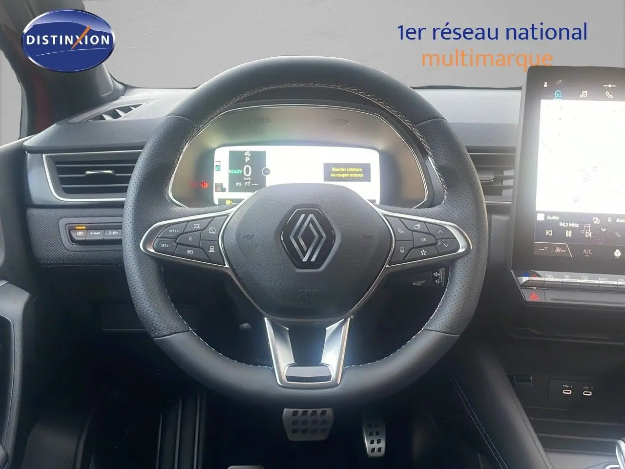 Vue intérieure centrée sur le volant noir perforé du Renault Captur E-Tech Hybrid 2025 avec tableau de bord digital et écran tactile.