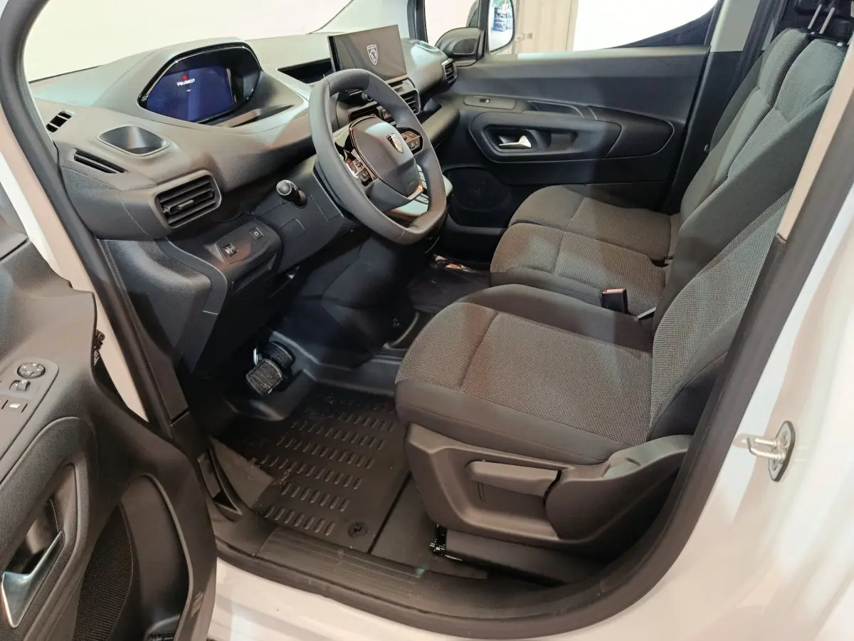 Vue intérieure côté conducteur du Peugeot Partner blanc 2025, montrant sièges tissu gris et tableau de bord moderne.
