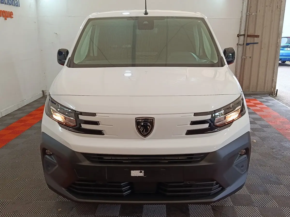 Vue frontale d'un Peugeot Partner XL blanc avec calandre noire et phares allumés en intérieur.