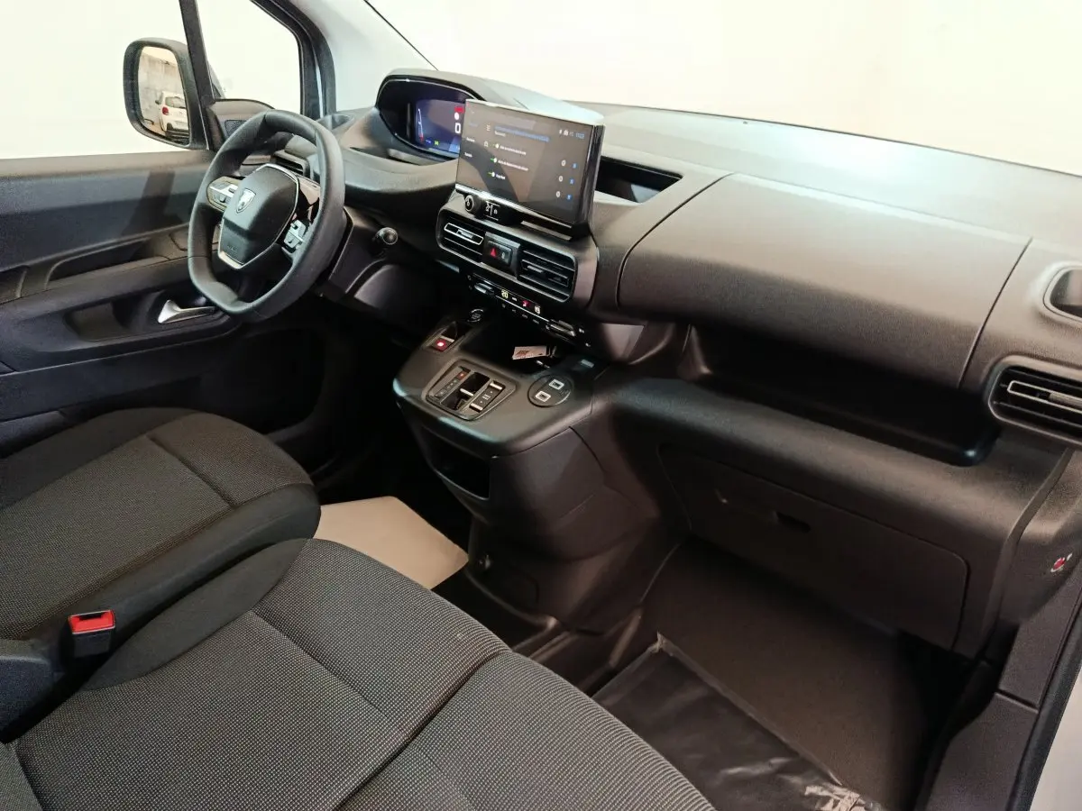 Intérieur du Peugeot Partner XL 2025 vu côté passager, tableau de bord noir avec écran tactile central et sièges gris foncé.