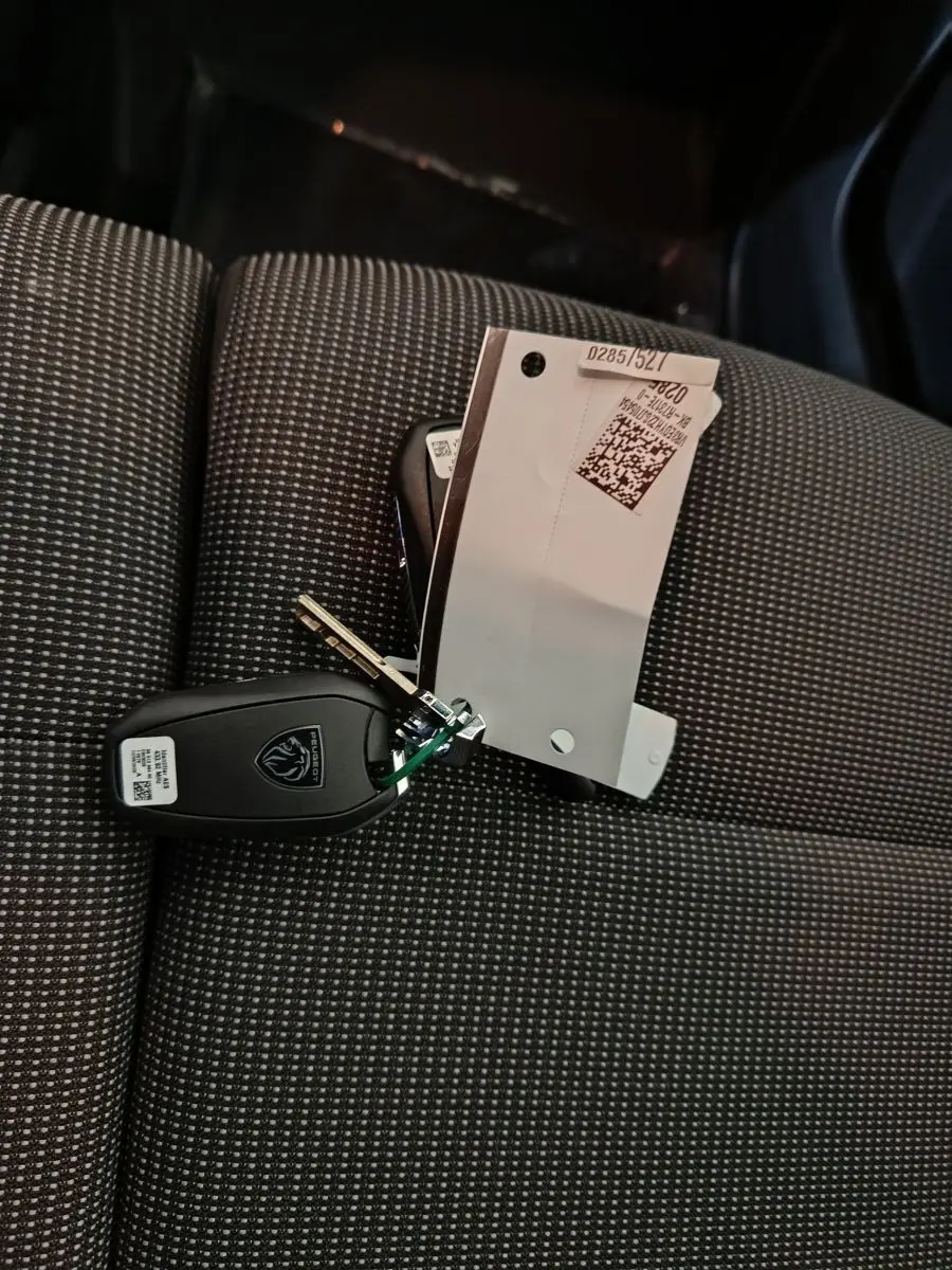 Clé Peugeot posée sur un siège avant gris à motifs, intérieur du Peugeot Partner XL 2025 visible en arrière-plan.